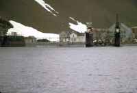 View from the deck of the RRS John Biscoe of the Stromness whaling station, South Georgia. A Gemini landing craft with Ricky Chinn, Captain Malcolm Phelps, Duncan Carse and Ship's Officer, has just beached. About midday, 7th November 1972.