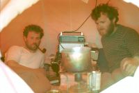 View inside the tent. Sleeping accommodation was by sleeping bags on top of air beds arranged on either side of the tent. In the centre, the primus stove was operated on top of the current sledging ration (food) box. An old (black painted) sledging box contained personal belongings. On top of that was the Squadcal radio tranceiver the aerial leading up to the ventilator in the roof of the tent. December 1972.