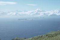 View looking east on Annenkov Island with the Spilite Arch promontory on the bottom left, the islands of the Hauge Reef in the middle-ground and South Georgia in the background. December 1972.