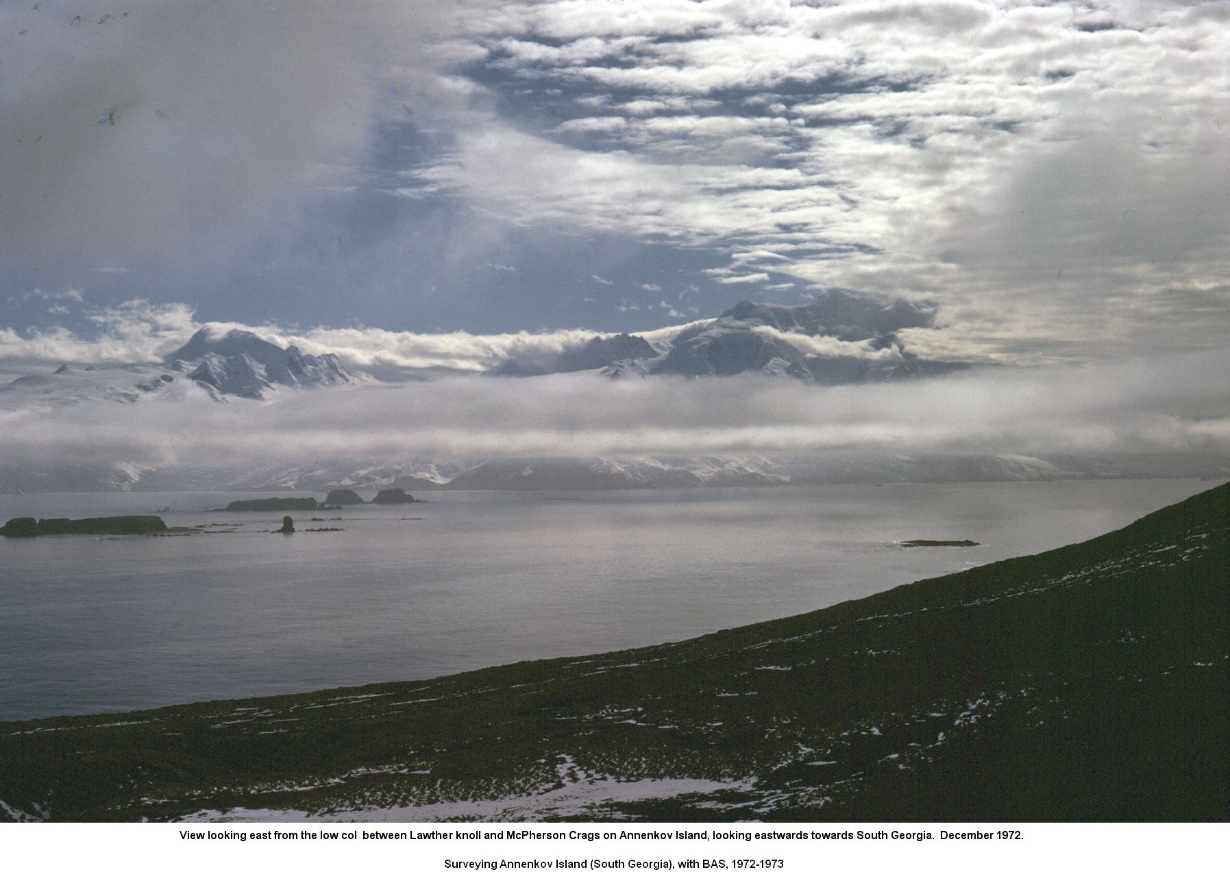 View looking east on Annenkov Island with the Spilite Arch promontory on the bottom left, the islands of the Hauge Reef in the middle-ground and South Georgia in the background.  December 1972.